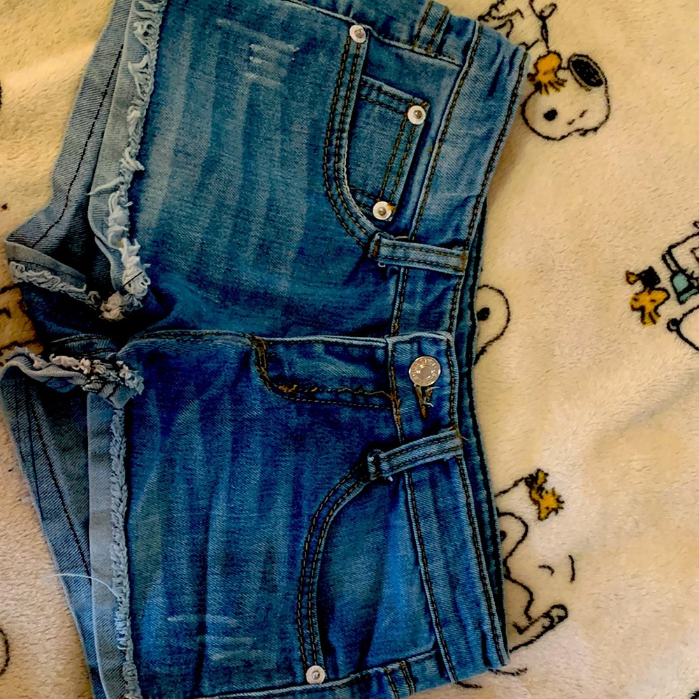 Girls low wasted Jean shorts wear on pockets, faux leather is cracked.